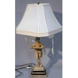A resin table lamp, with white material shade on brass style column fronted by a figure holding a