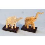 A matched pair of early 20thC ivory figures of elephants, each with trunks raised on rectangular