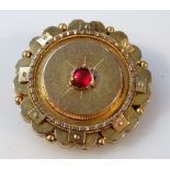 An early 20thC memorial brooch, floral set, centred by a red stone, part yellow metal with plain pin