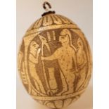 A heavily carved ostrich egg, decorated with panels of various figures with an upper and lower