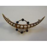 A crescent shaped brooch, set with seed pearls through a blue stone set in yellow metal.