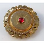 An early 20thC memorial brooch, floral set, centred by a red stone, part yellow metal with plain pin