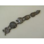 A coin bracelet, made up of a number of various hammered coins joined by chain links, unmarked white