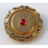 An early 20thC memorial brooch, floral set, centred by a red stone, part yellow metal with plain pin