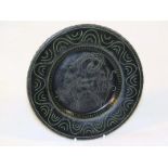 A 20thC Studio plate, sgraffito decorated with a goat with a green and dot line border, on a black
