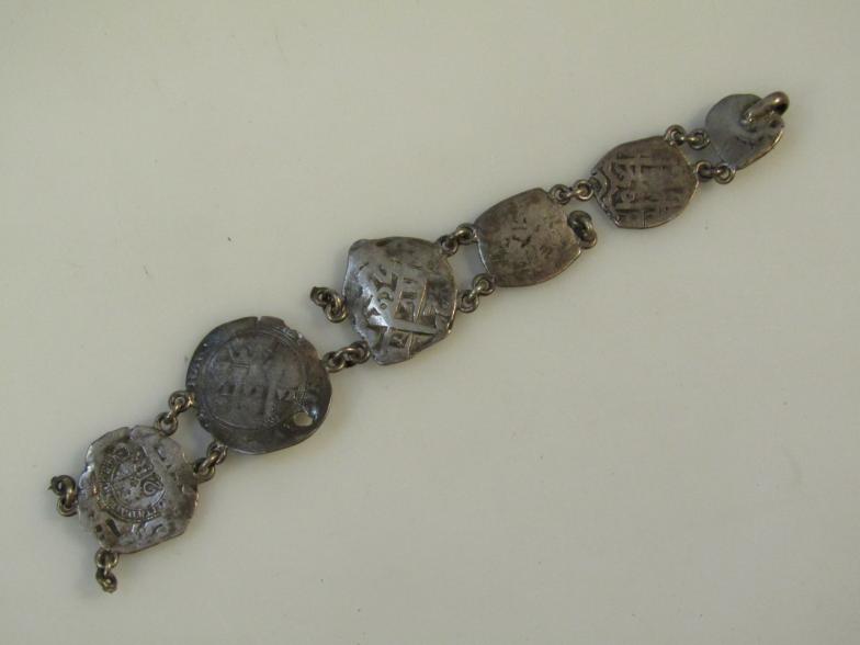 A coin bracelet, made up of a number of various hammered coins joined by chain links, unmarked white