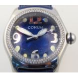 A modern Corum bulls eye ladies wristwatch, with blue dial, and gem encrusted surround, on blue