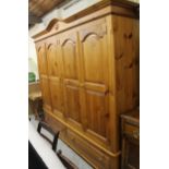 A modern stripped and lightly polished pine triple door wardrobe, with a fixed cornice centred by