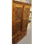 A JIG style hardwood TV cabinet, with a overhanging top above two meshwork doors and four drawers