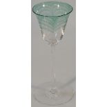 A wine glass, the bell shaped bowl with green flecks on a slender cylindrical stem terminating in
