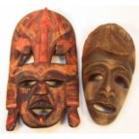 Two 20thC African tribal hardwood masks, each part pierced, the first highlighted in red with a