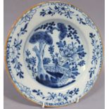 An 18thC blue and white tin glazed earthenware plate, the centre decorated with trees, flowers and