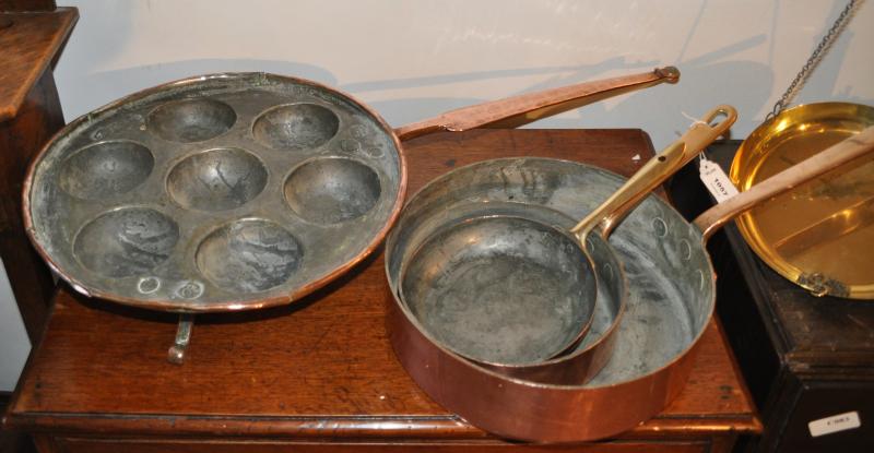 A copper seven egg poacher together with three copper frying pans