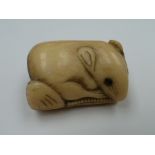 A carved bone netsuke in the form of a rat on a bed of leaves, unsigned, 2cm high.