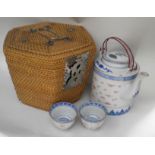 A Chinese rice grain porcelain teapot with two bowls in a carrying basket.