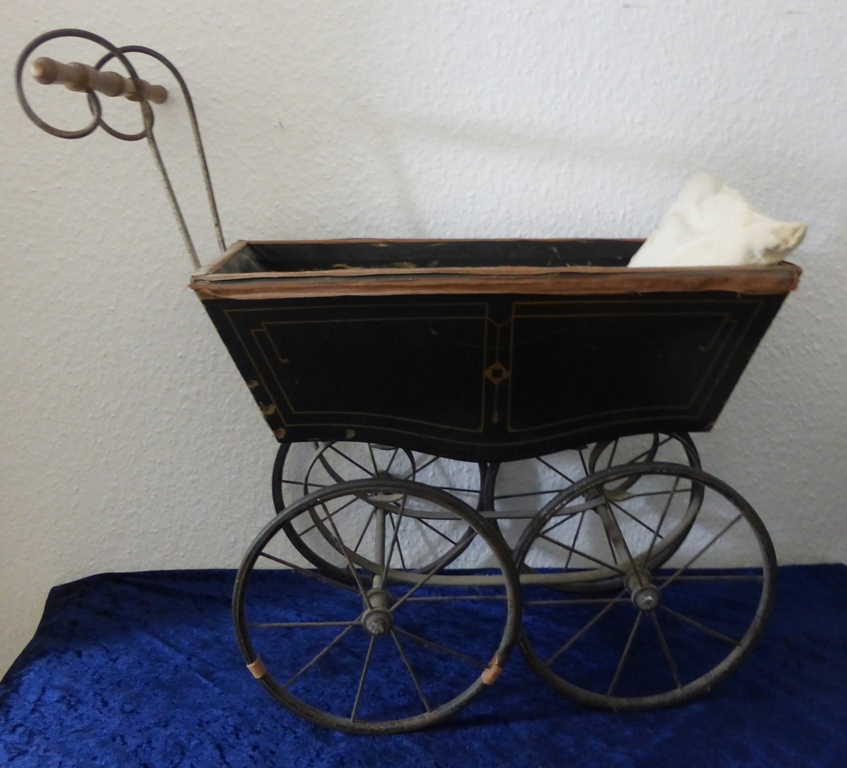 Puppenwagen um 1920, schwarz lackiertes Holz, auf Eisenrädern, geschwungene Lenkstange, l.63cm, h.