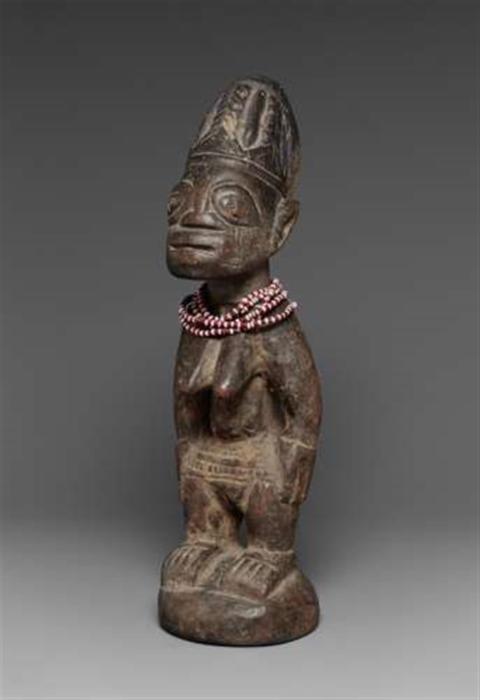 A YORUBA FEMALE TWIN FIGURE  Ibeji, white and red beads about the neck, dark patina. 31 cm.