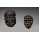 TWO IBIBIO MASKS  Each with carved teeth in the open mouth, the smaller depicting a yaws sufferer,