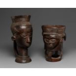 TWO KUBA CUPS  Each carved as a head, one on pierced openwork base, the other on ringed neck, dark