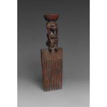 A CHOKWE COMB  With hatched panel above the nine tines, surmounted by a crouching female figure with