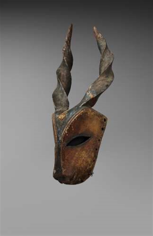 AN OGONI ANTELOPE MASK  With spiral horns and large pierced eyes, painted yellow and blue. 49 cm.