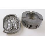 Two vintage aluminium ashtrays, one a the top of a piston and the second with two figures and the