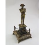 A brass figure of napolean standing arms folded atop a plinth mounted on a marble stand that in turn