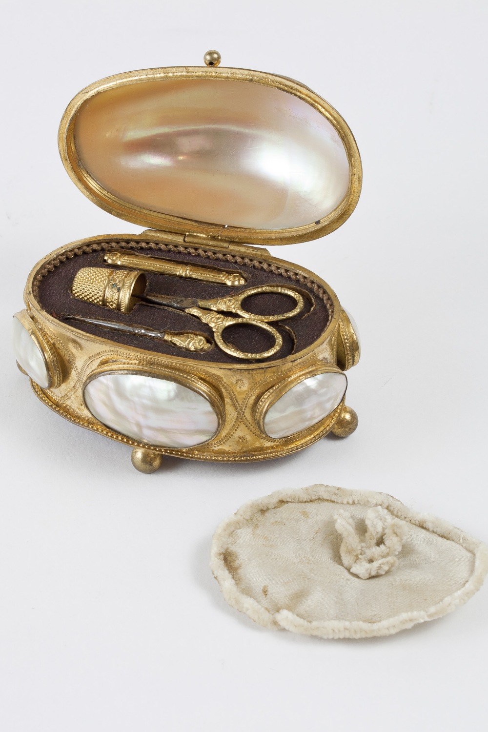 Small oval box in golden metal for sewing accessories. Mother-of-pearl lid and elements on the box’s