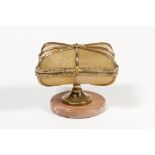 Casket in the shape of a cushion. It is made out of blonde shells in a bronze structure and rests on