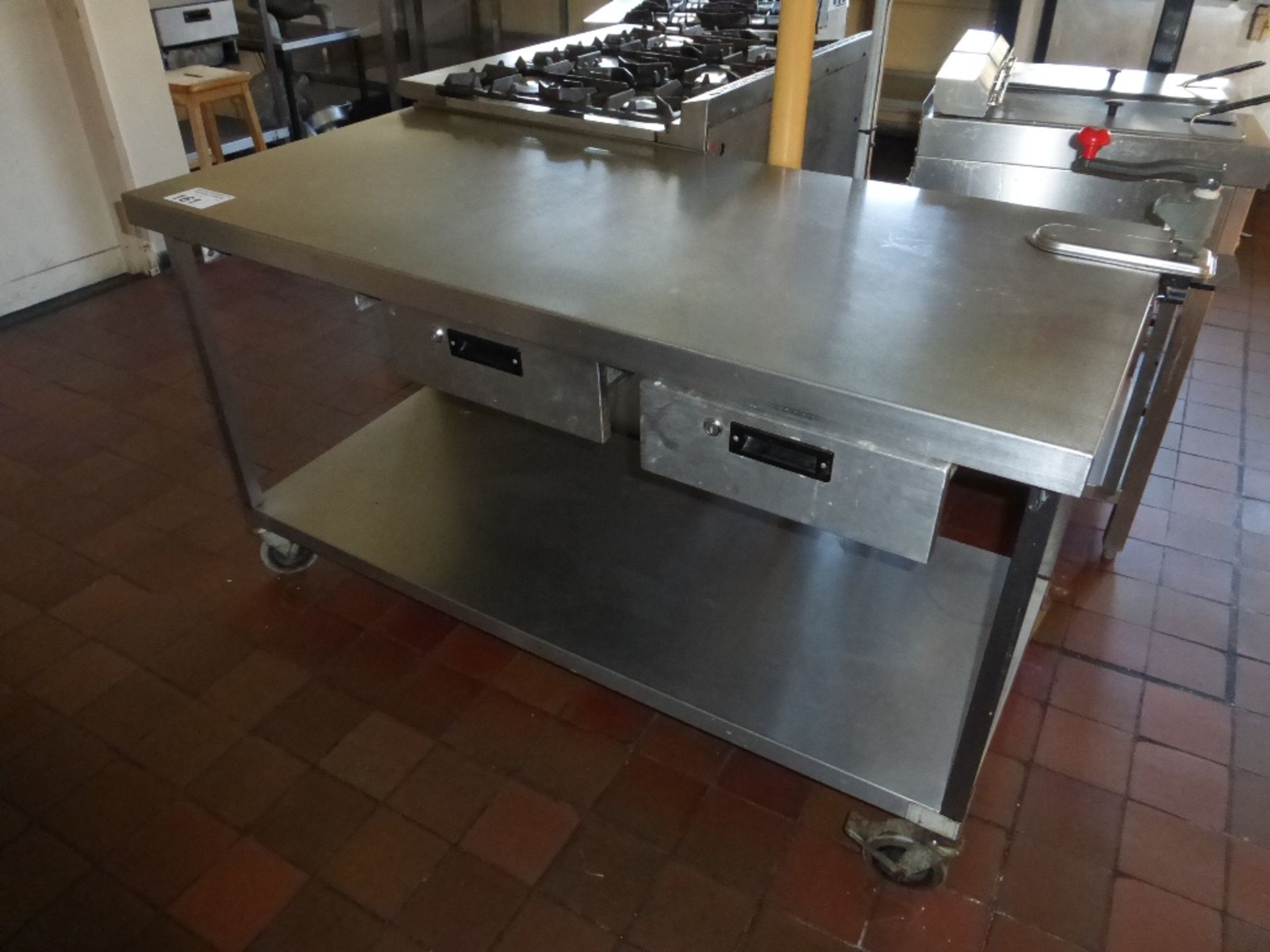 1 rectangular topped stainless steel mobile kitchen table with two drawers and a can opener (located