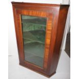 NV- A mahogany wall hanging corner cabinet with a glass door enclosing a painted shelves