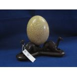 African ostrich egg on carved wooden stand having camel mounts.