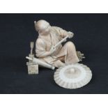 JAPANESE CARVED IVORY OKIMONO TYPE FIGURE OF A PARASOL SELLER RECLINING WITH HIS WARES.  Two