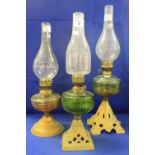 Three similar early 20th Century oil lamps, one with green glass reservoir.