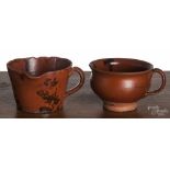 Two Pennsylvania redware handled cups, 19th c., with manganese splotching, one with a spout, 3" h.