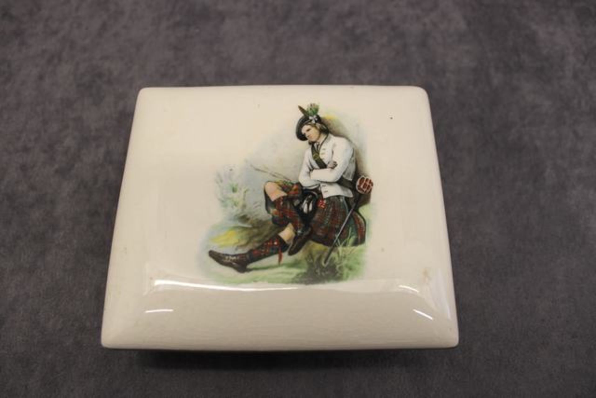 A porcelain trinket box and cover , early 20th Century,  decorated with a Scottish man resting,  a