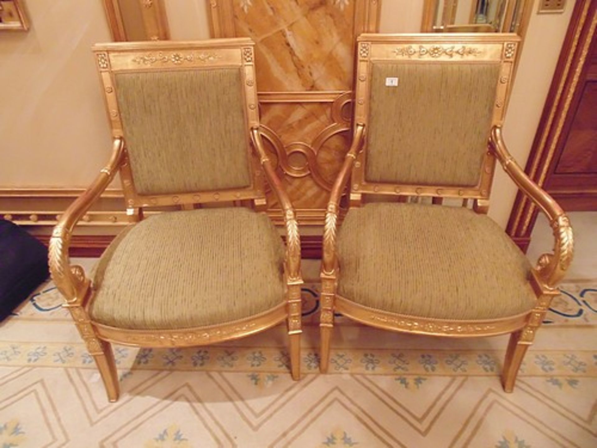 A pair of Empire style giltwood armchairs the back rest with panelled top rail decorated with