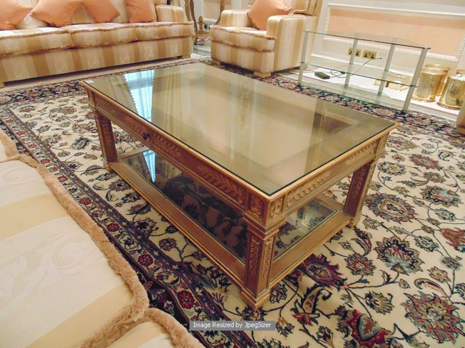 A wood carved coffee table with a centre frieze pull out drawer below a glass inset top with a