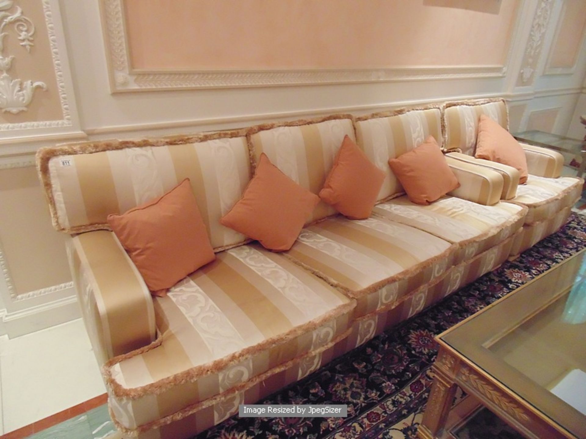 An upholstered heavily padded three seater sofa upholstered in cream and gold with a frill edging