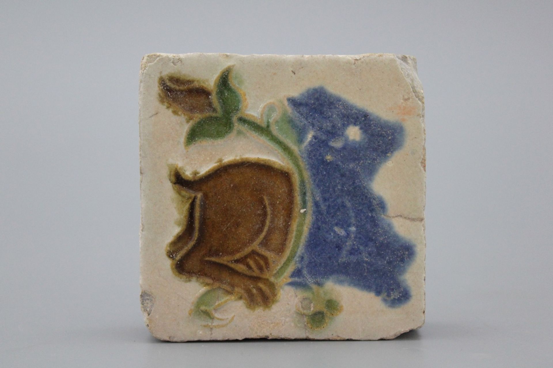 A Spanish olambrilla tile, Seville, first half 16th C. Decorated in relief with a beast and a flower