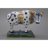 A polychrome Dutch Delft cow, 18th C. Naturalistically modelled on a green and blue base with frogs.