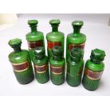 Four ribbed green glass pharmaceutical bottles all with red and gold labels, 8 ins high (20 cms)