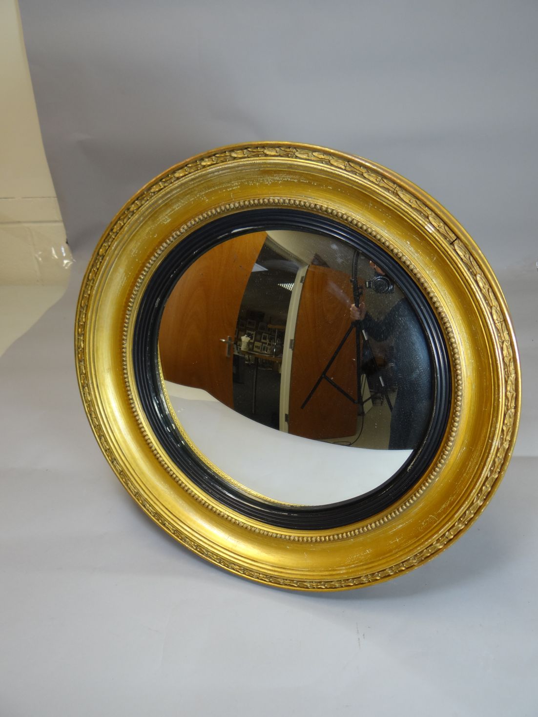 A circular gilt framed convex mirror with ebonised slip and laurel border, 20 ins diam (51cms)