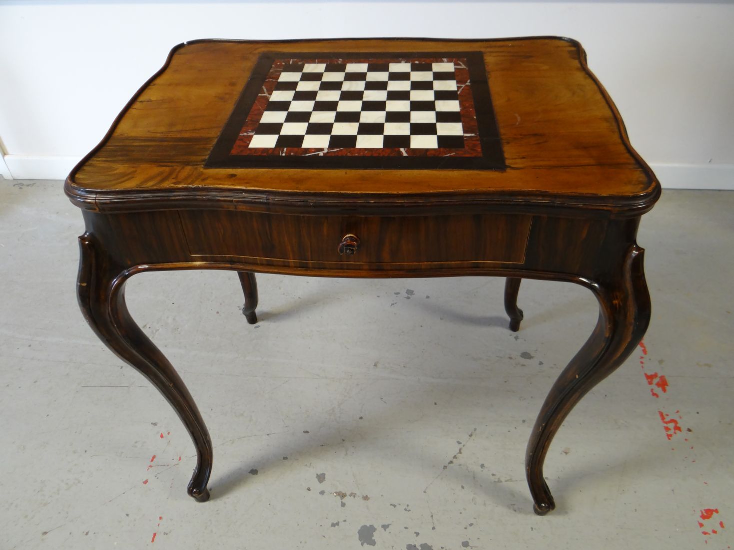 An antique multi-wood galleried shaped games-table, having an inset marble chequer board on bow-legs