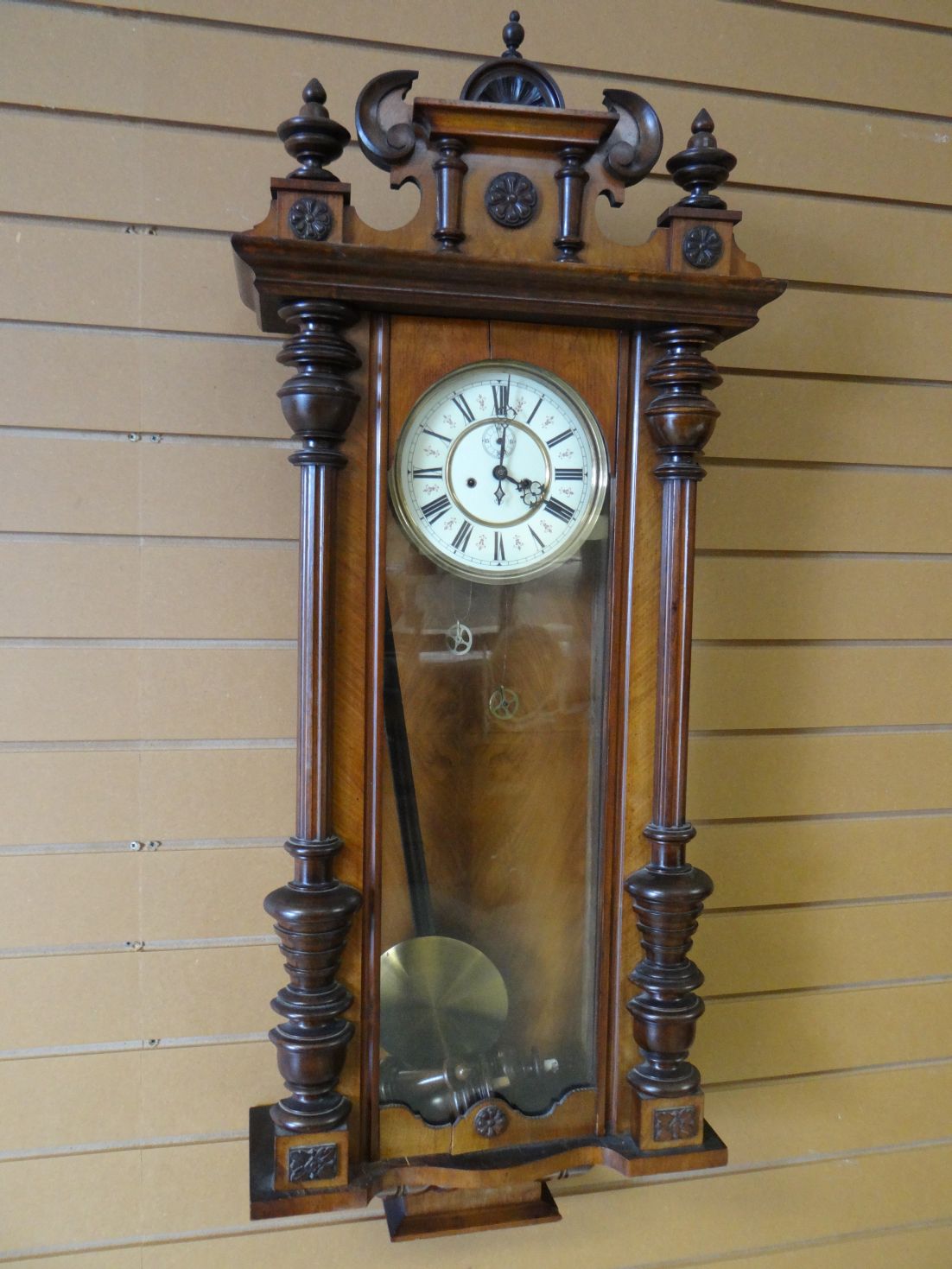 A full Vienna type multi-wood wall clock with ornate pediment and Gothic-style Roman Numeral dial,