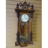 A full Vienna type multi-wood wall clock with ornate pediment and Gothic-style Roman Numeral dial,
