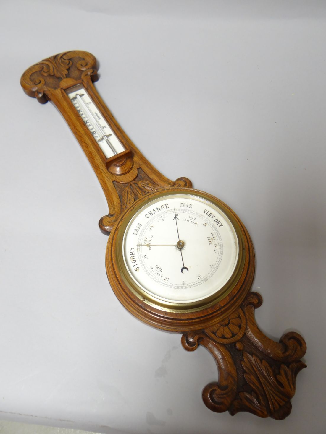 A carved oak encased banjo aneroid barometer, with printed dial and brass bezel, 27.5 ins long (70