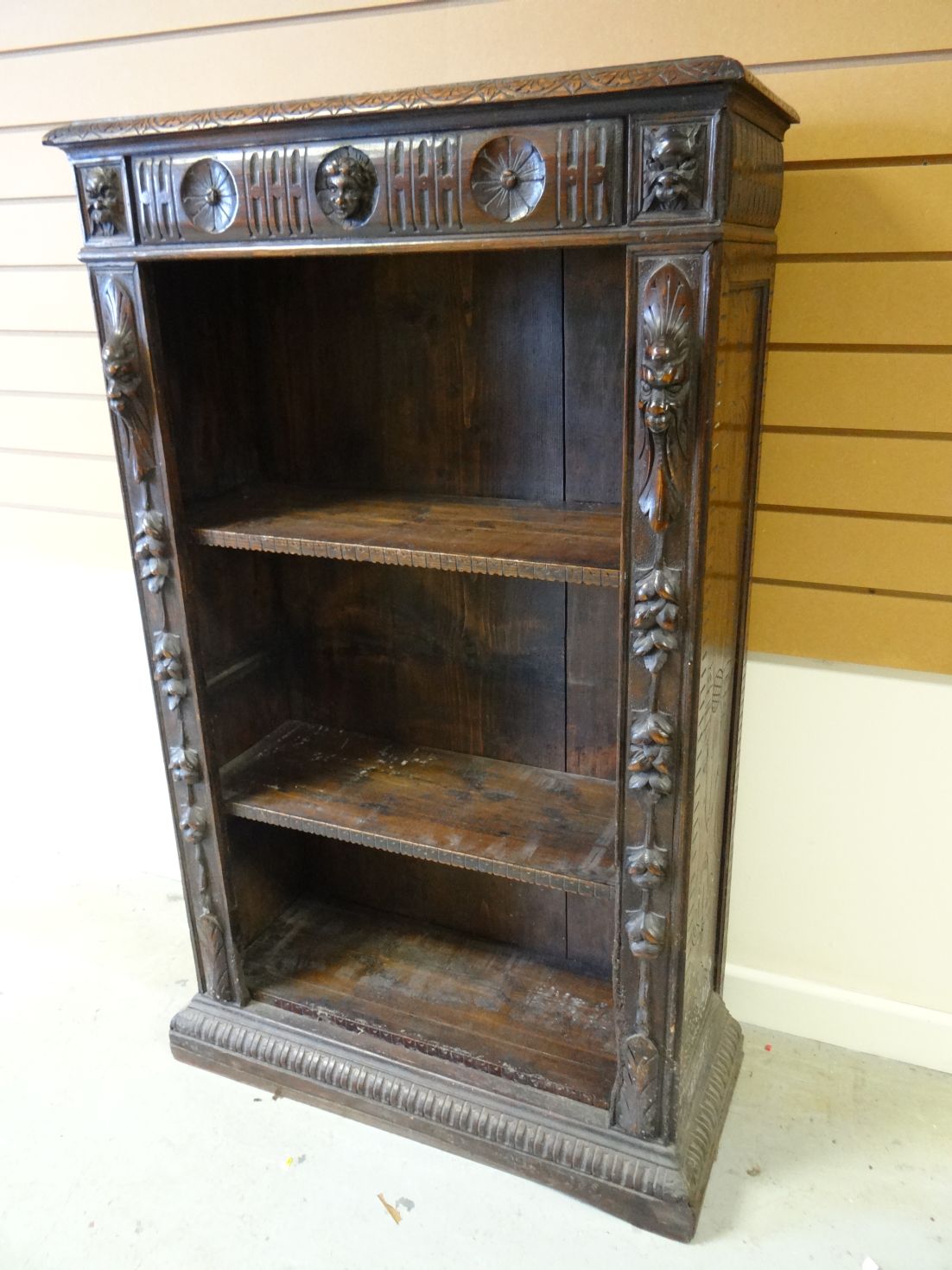 An early twentieth century stained open bookcase profusely carved with lunettes, rosettes and masks,