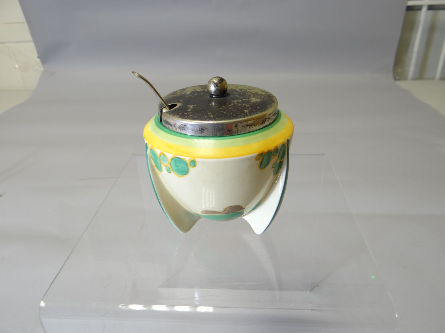 A Clarice Cliff tri-footed and EPNS lidded preserve pot painted with red roofed cottages in a