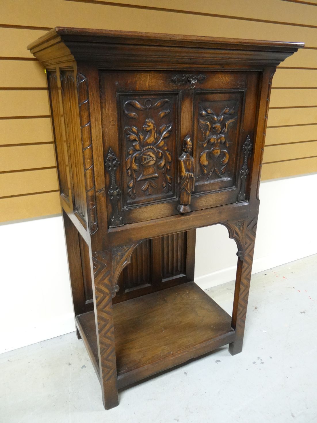 A dark wood Gothic- style raised cupboard with fall-front single door above a lower tier. 51 ins